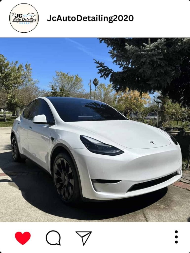 A white Tesla Model Y, recently detailed, parked in a driveway. The car has black accents and chrome details