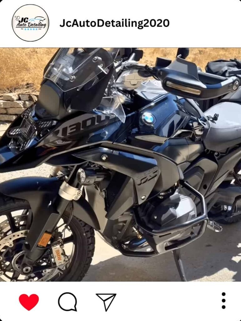 A black BMW R1300GS adventure motorcycle, recently detailed, parked on a driveway. The motorcycle has additional accessories like panniers and a windshield.