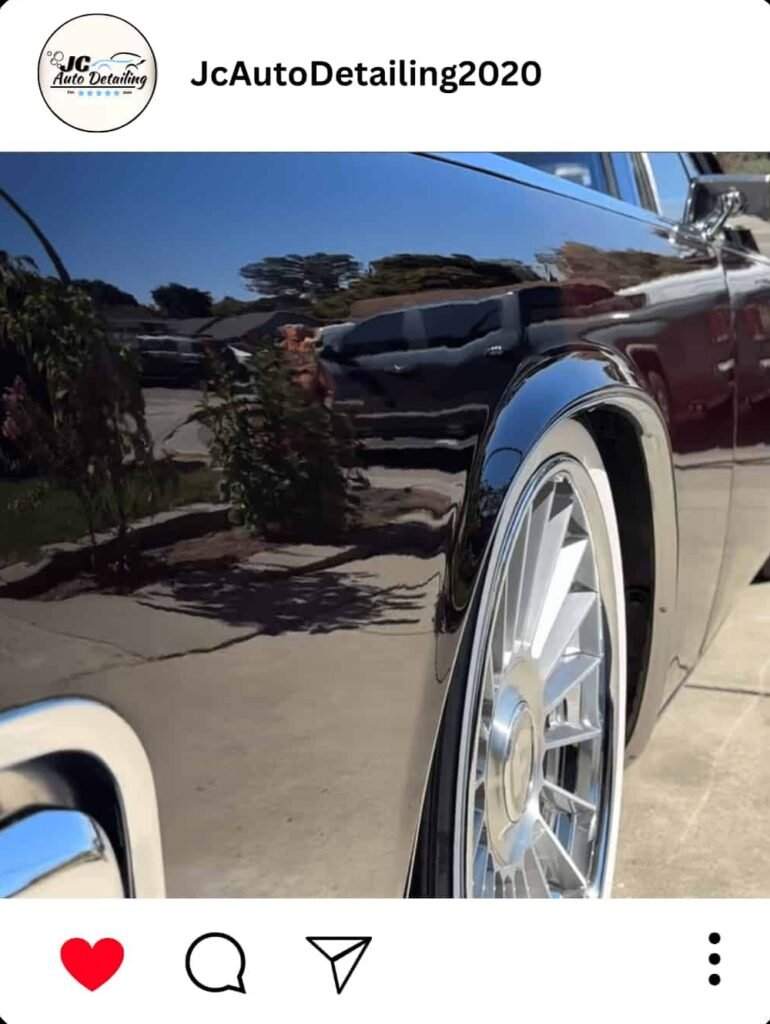 A close-up of the back of a black classic car. The car has custom chrome wheels and a highly polished paint job that reflects the surroundings.